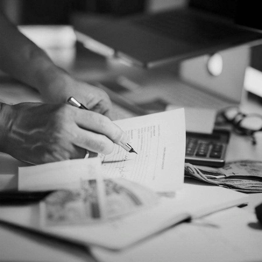 Detalle de una firma sobre un documento, con calculadora al fondo